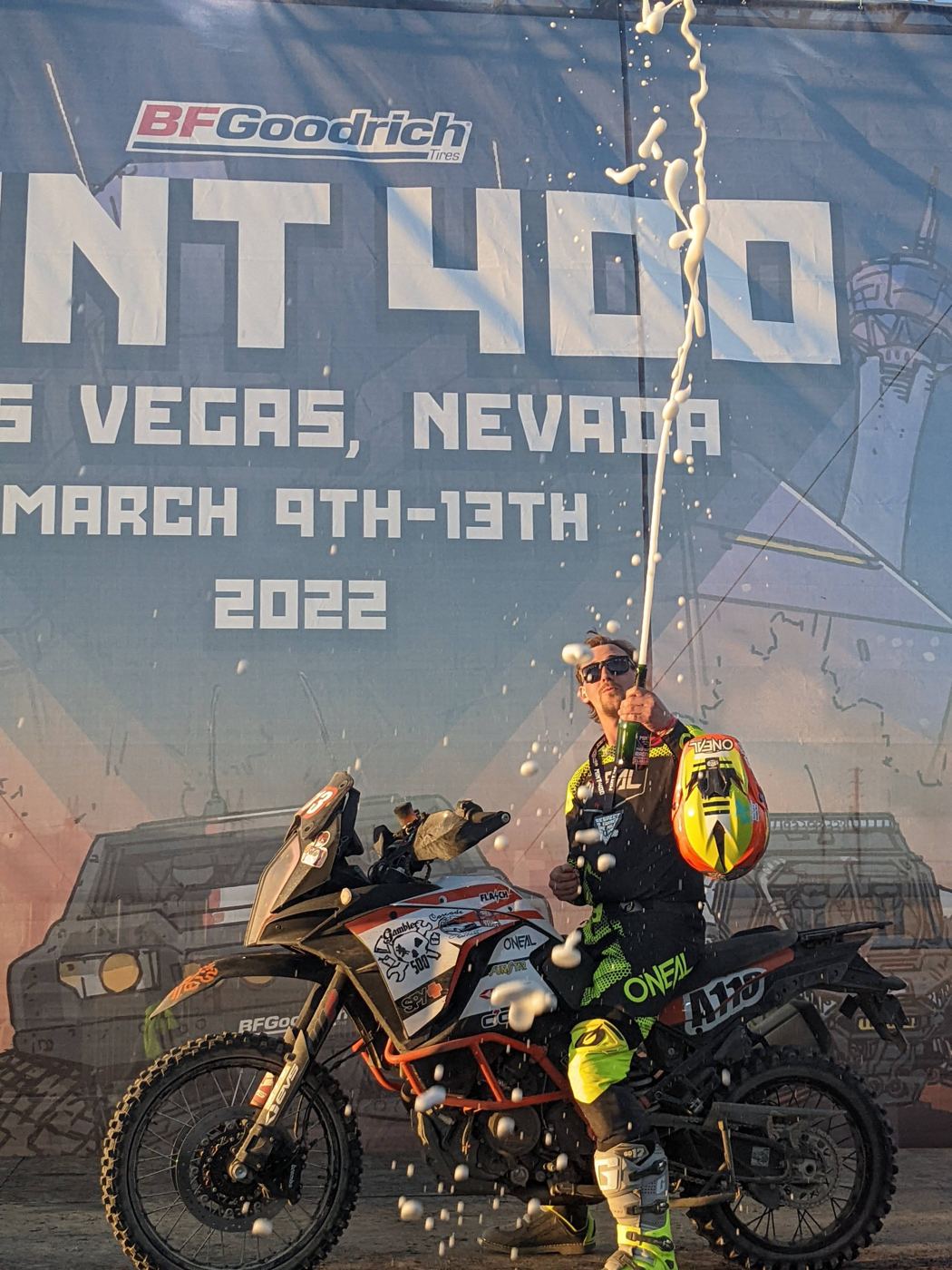 Spraying champagne on the KTM in front of the 2022 Mint 400 banner