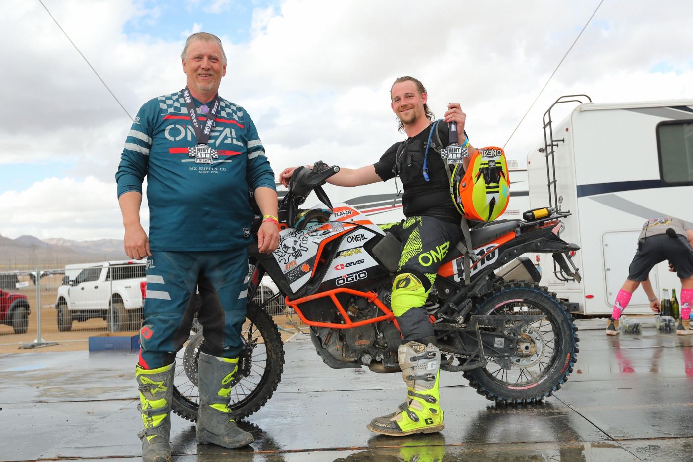 Two riders with Mint 400 finisher medals beside the KTM